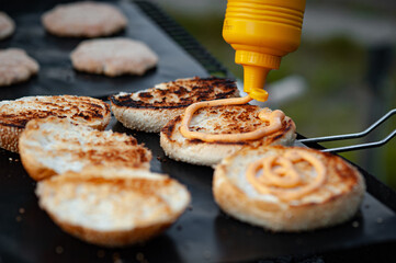 Cooking a burger on the grill. Spreading sauce on a burger bun