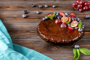chocolate homemade cake with fresh blueberries and red grapes, mint on a wooden brown background, blue towel, berry pie,