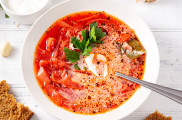Russian cuisine, traditional  vegetable soup, borscht with sour cream and parsley in a white plate, spoon,  on a white