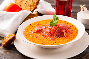 traditional russian  borscht with sour cream and parsley in a white plate, tomatoes on a  wooden background, red  soup, glass juice