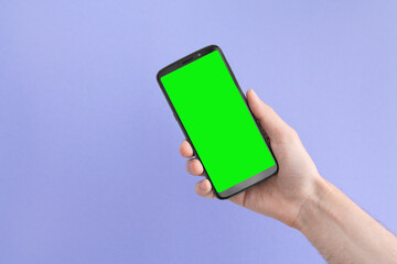 Smartphone with a green screen in right hand on an lilac background, angled position.