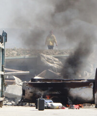 Fireman in background of emergency accident with boulders, smoke, fire and burnt metal in foreground