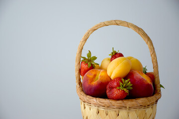Farm basket filled with various colorful fruits and berries on white table: peaches, strawberry and...