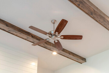 Fototapeta Ceiling fan with lights between decorative wood beams inside living room of home obraz