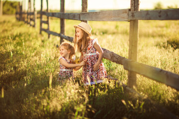 children, girls in hat standing next to fence in village. walks in countryside.