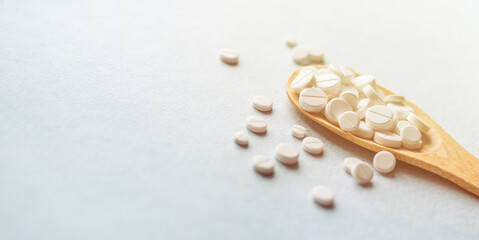 Close-up white pills, tablets in wooden spoon on blue table in the rays of sunlight. Medicine and health concept. Pharmaceutics. Pills and vitamins