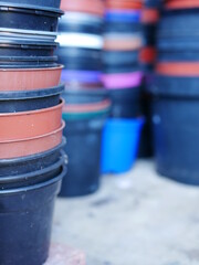 Stack of round multi coloured plastic flower pots with more stacks In background