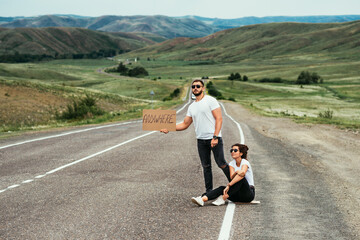 A couple hitchhiking. A man and a woman catch a car by the road. A young couple votes on the road. A man and a woman are hitchhiking. A couple hitch a ride on the road. Hitching a ride. Copy space