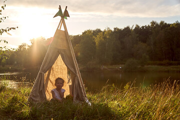 A little girl is sitting by the lake. Sunny akat. Wigwam. Happy child. High quality photo