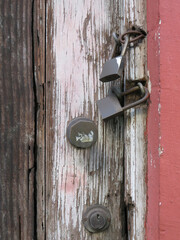 Padlocks and rusty iron chain on broken white old wooden door with violet graffiti. Locks on a chain hangs on a door. Old metal padlocks on a uncorked wooden door.