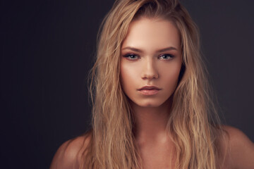 Fototapeta premium Closeup face portrait of young pretty caucasian woman with long blonde woman looking in camera and posing against gray background. Shallow DOF.