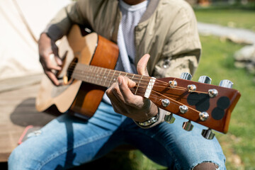 Close-up of unrecognizable musician playing acoustic guitar outdoors while enjoying camping