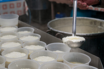 Fototapeta na wymiar The making of ricotta cheese: farmer filling small plastic containers with hot ricotta cheese