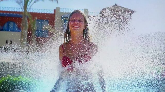 Slow motion of summer season for girl relax in swimming pool with water fountain under waterfalls to swim in splashing water and sun sparks . Large drops of water fall on young woman .