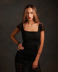 Body length studio portrait of young attractive woman with brown long hair posing against gray wall in dark interior