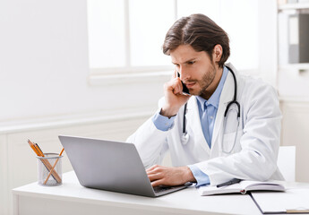 Focused doctor looking on results on laptop and talking on phone