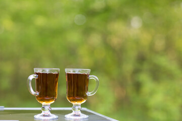 Two beautiful glass glasses with black tea on nature on a natural green background