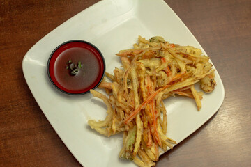 Tempurá de legumes frito acompanhado de molho de soja (shoyu), servido em prato branco