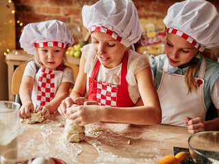 Three little chefs enjoying in the kitchen making cakes. Girls at the kitchen. Family housekeeping