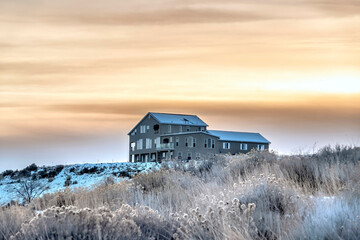 Home sitting on snowy hill with golden cloudy winter sky background at sunset