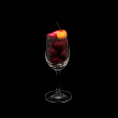 Cherries in a glass against black background, still life with red and yellow fruit 