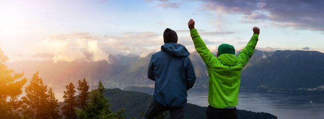Fototapeta premium Adventurous Friends on top of a Mountain Top with Hands up. Sunset or Sunrise Composite. Background from Bowen Island, British Columbia, Canada.
