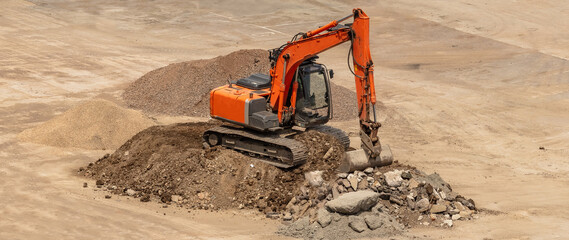 Old orange excavator parked on top of a pile of soil and ready to dig. Rocks lying around....