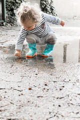 petite fille joue dans une flaque d'eau avec ses bottes