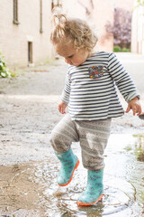 petite fille joue dans une flaque d'eau avec ses bottes