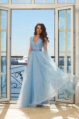 Young beautiful stunning girl in long blue dress posing in interior with open door and view on...