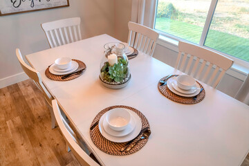 Dining table with tableware centerpice and chairs against brown wood floor