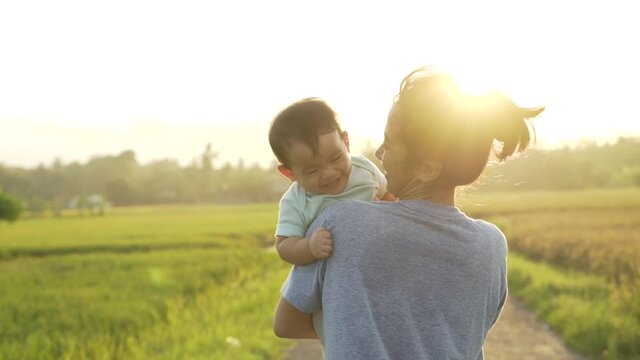 happy mother and baby playing together outdoor enjoy beautiful sunset in the field