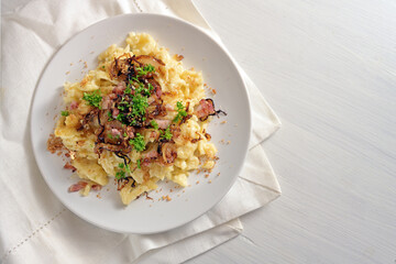 Spaetzle, homemade egg noodles with cheese, roasted bacon, onion and breadcrumbs, with parsley garnish on a white table, traditional in Germany and Austria, copy space, high angle view from above