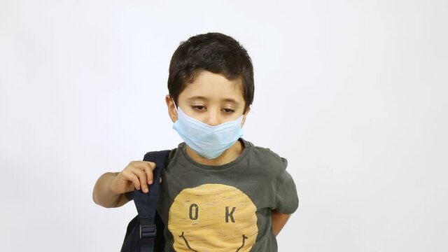 Back to school after Corona - 5 years old boy wearing face stands up and put on back bag waving goodbye