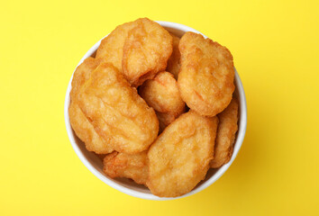 Bucket with tasty chicken nuggets on yellow background, top view