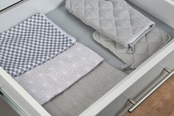 Open drawer with folded towels and oven mittens. Order in kitchen