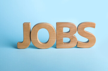 Word JOBS made with wooden letters on light blue background. Career concept