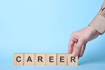 Woman making word CAREER with wooden cubes on light blue background, closeup. Space for text