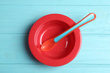Fototapeta na wymiar Plastic plate and spoon on light blue wooden table, top view. Serving baby food