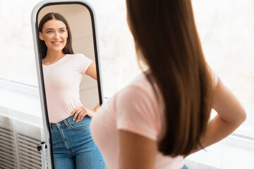 Smiling Girl Looking At Mirror After Slimming Standing Indoors