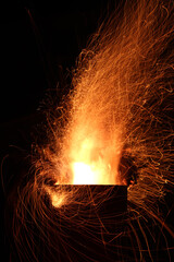 Flames of fire and sparks from firewood burning in a metal outside fireplace at night against a dark sky