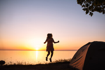 Girl meets the sunrise near the tent on the sea