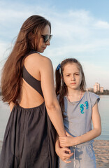 Fototapeta na wymiar Mother and daughter are standing on the shore of the lake. The girl looks towards the camera, and the woman looks at her daughter. Both have long hair and pleasant features. High quality photo