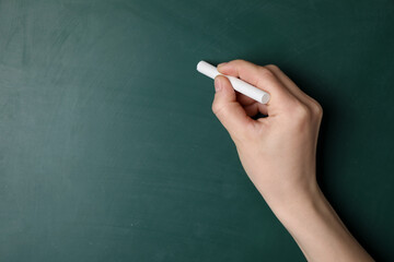 Woman with white chalk near green blackboard, closeup. Space for text