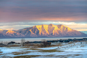 Snowy mountain lit by golden sun at sunset with lake and homes in the foreground