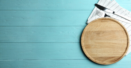 Wooden plate with cutlery and napkin on light blue table, flat lay. Space for text