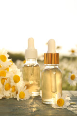 Bottles of essential oil and chamomiles on blue wooden table in field