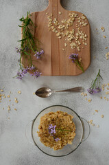 Top view wooden cutting board oatmeal porridge and lilac spring flowers/ Breakfast concept