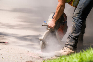 Asphalt cutter. A worker cuts through an asphalt road with a large handheld rotary cutter. Lots of...