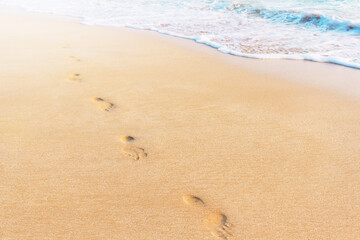 Footprints in the sand and soft sea wave on the beach background. Sunshine and copy space for text. Travel, summer holidays and vacation concept photo.